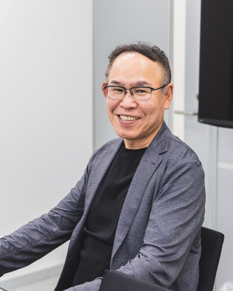 椅子に腰かけ、こちらを見て笑う桑原社長
