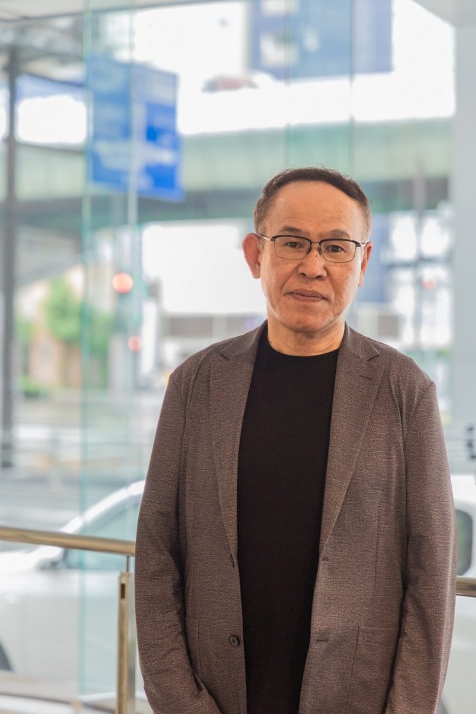 ガラス張りのエントランスを背に立つ桑原社長